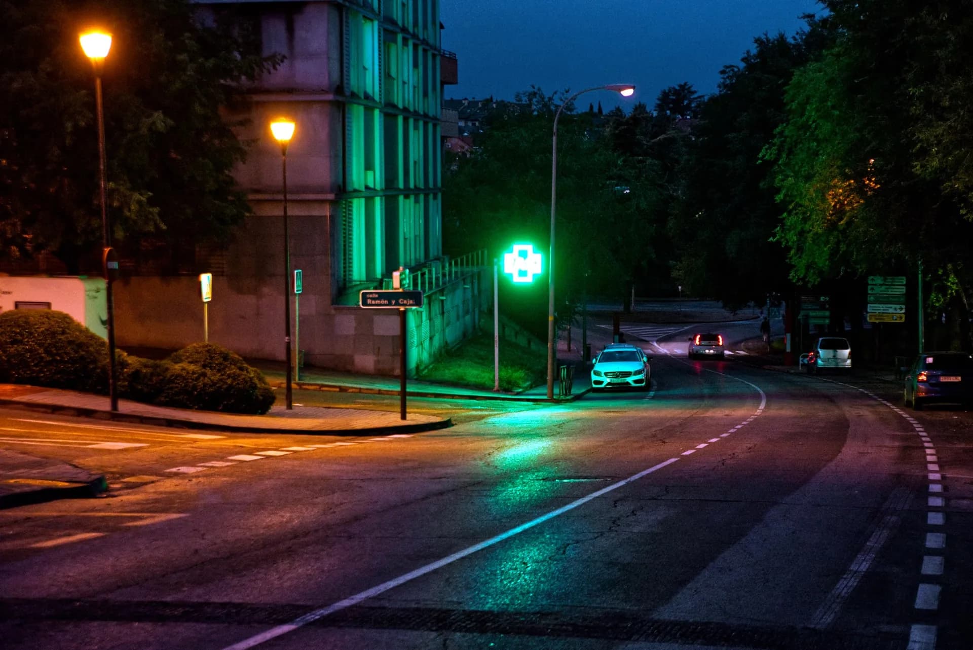 A quiet street corner at night, lit by a glowing green neon sign.